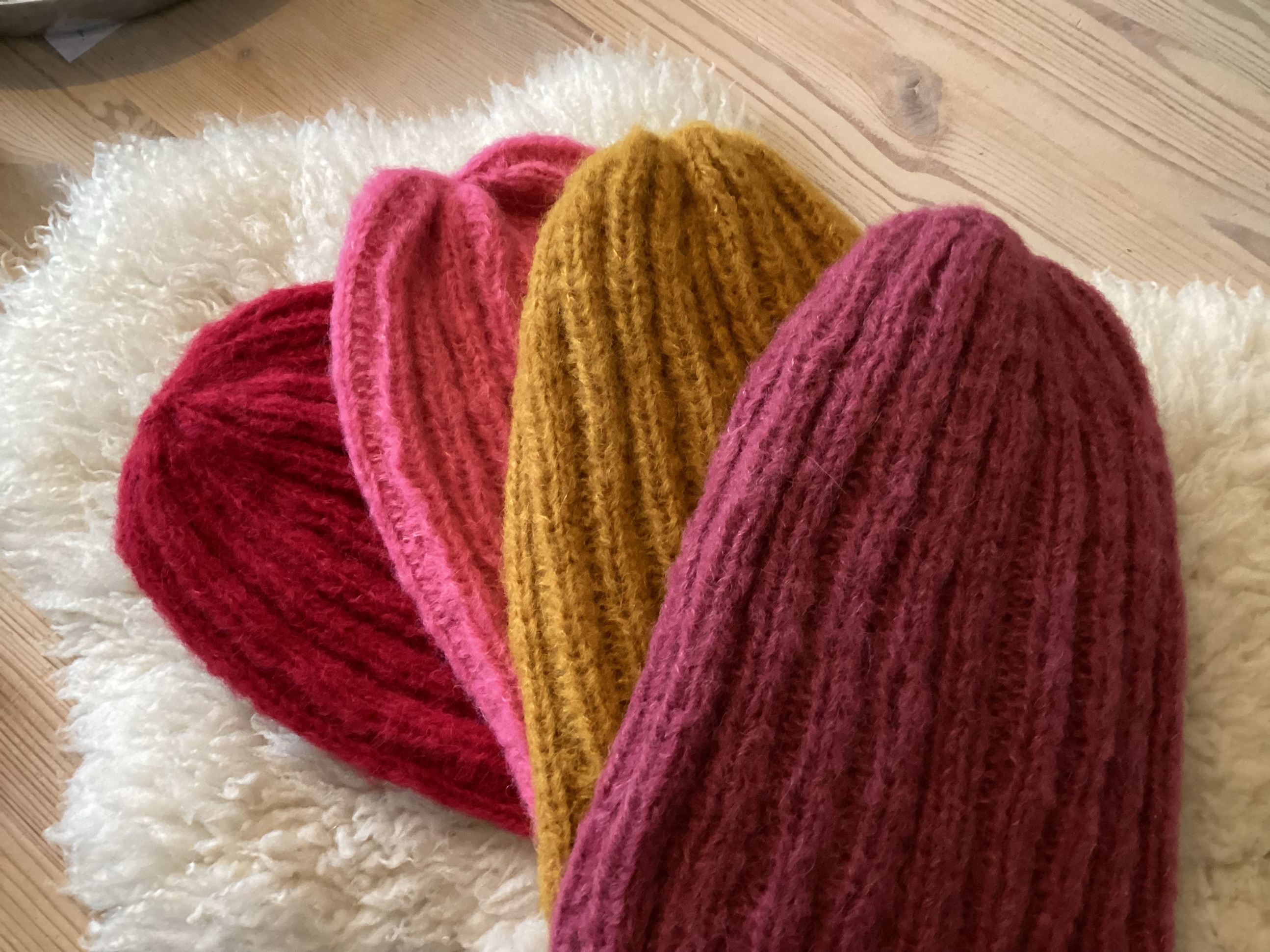 Vier handgestrickte Mützen in Rot, Pink, Senfgelb und Beere